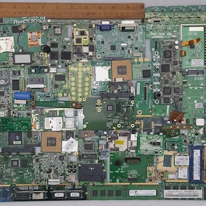 May include: A collection of various green circuit boards with integrated circuits, chips, and other electronic components. A wooden ruler is placed across the top. The boards are arranged in a rectangular shape.