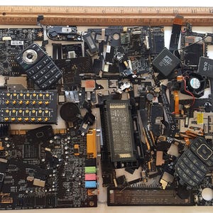 May include: A collection of black circuit boards, chips, and other electronic components. The components are arranged in a random pattern on a white surface. Some of the components have gold-colored contacts. There are two cell phones in the image, one with a black and silver case and the other with a black case. The text "Sound Lively" is visible on one of the circuit boards.