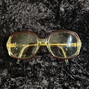 May include: Brown and yellow plastic framed glasses with the text "Nina Ricci" on the side.