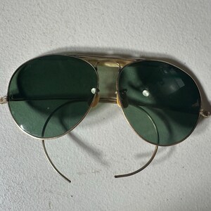 Op de afbeelding: Gouden aviator zonnebril met donkergroene glazen en dunne metalen frames.