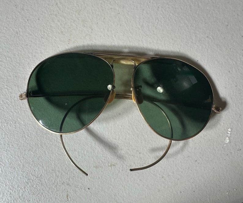 Op de afbeelding: Gouden aviator zonnebril met donkergroene glazen en dunne metalen frames.