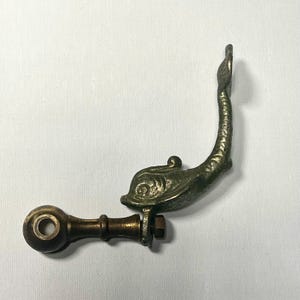 May include: A vintage metal dolphin-shaped door handle with a round knob and a screw attachment. The handle is painted in a green and gold color.