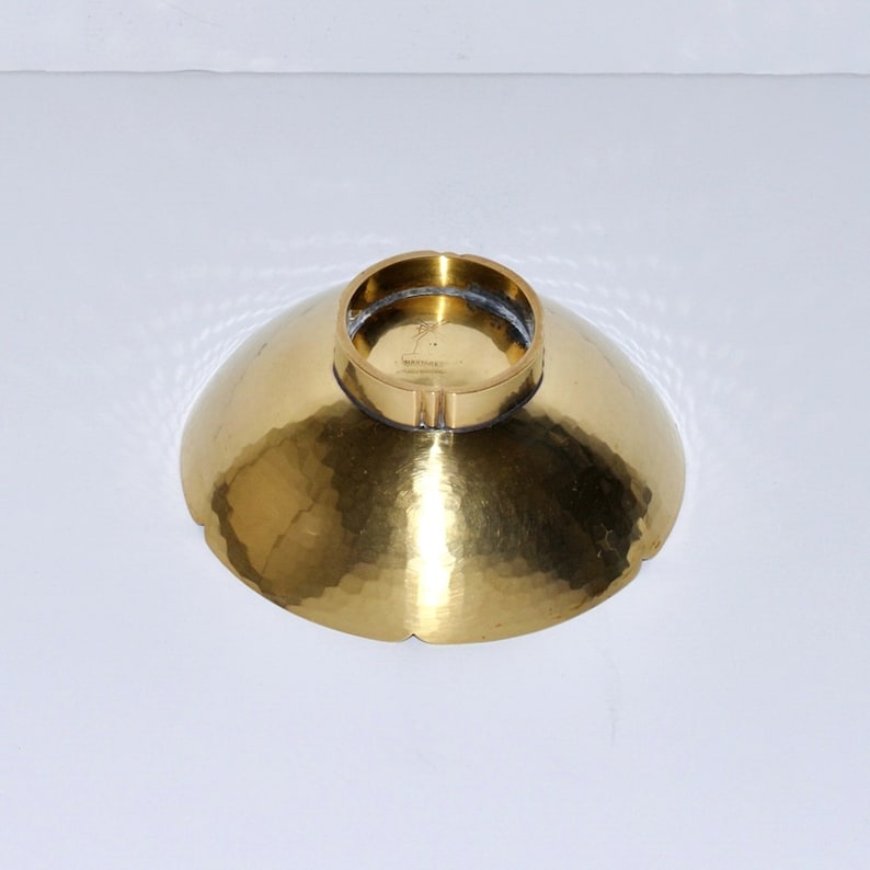 Puede incluir: Un cuenco de metal martillado dorado con un borde festoneado. El cuenco tiene un borde elevado y un interior liso y pulido. El fondo del cuenco tiene una marca del fabricante.