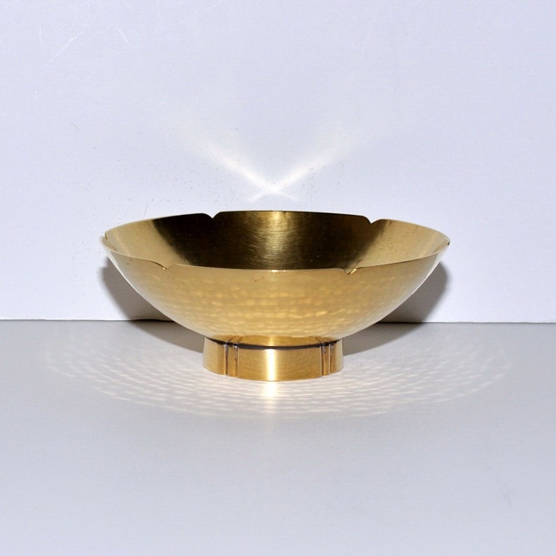 Puede incluir: Un cuenco de metal dorado martillado con un borde festoneado y una base corta y cil&iacute;ndrica.