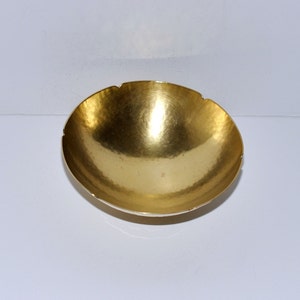 Puede incluir: Un cuenco de metal de color dorado con un borde festoneado. El cuenco es liso y brillante, y tiene una textura ligeramente martillada.