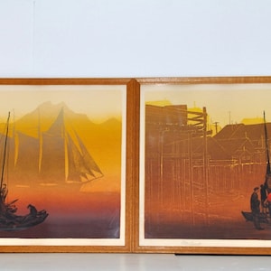May include: Two framed prints of a seascape with a sailboat in the distance and a small boat in the foreground. The prints are in a warm color palette of yellow, orange, and brown.