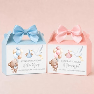 Può includere: Due scatole regalo, una blu e una rosa, con fiocchi di raso. Ogni scatola presenta un'illustrazione ad acquerello di una cicogna che trasporta un bambino, palloncini e un orsacchiotto. Il testo recita "Congratulazioni Un nuovo bambino/bambina".