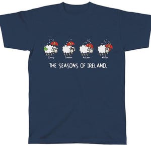 Könnte beinhalten: Ein marineblaues T-Shirt mit einer Grafik von vier Schafen, die die Jahreszeiten Irlands repräsentieren. Die Schafe tragen Regenschirme und haben verschiedene Accessoires für jede Jahreszeit. Der Text "The Seasons of Ireland" ist unter den Schafen gedruckt.