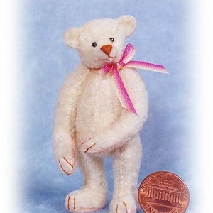 May include: A small, white teddy bear with a pink ribbon around its neck. The bear is standing next to a UK penny.