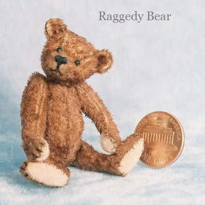 May include: A brown, plush, Raggedy Bear sitting on a light blue surface. The bear is about the size of a US penny, which is shown next to it.