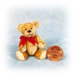 May include: A small, tan teddy bear with a red ribbon around its neck sits next to a penny. The bear has a stitched nose and small black eyes. Its paws and the tips of its ears are a lighter shade of tan. The penny reads "One Cent".