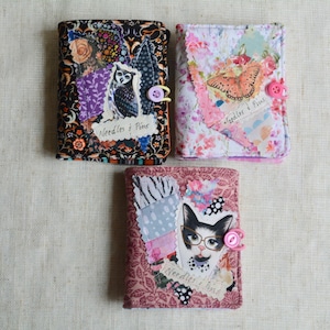 May include: Three fabric needle cases with patchwork designs. One features an owl, another a butterfly, and the third a cat wearing glasses. Each case has a button closure and the text "Needles & Pins".