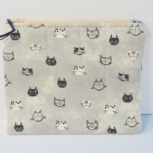 May include: A grey zippered pouch with a repeating pattern of black and white cat faces. The pouch is made of a soft, quilted fabric.