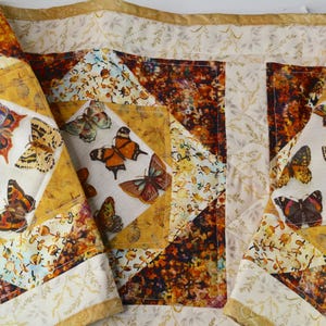 May include: A patchwork quilt with a butterfly theme. The quilt features a variety of butterfly designs in shades of orange, yellow, brown, and purple. The quilt is made of fabric with floral and geometric patterns.