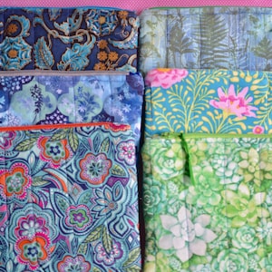 May include: A collection of six quilted fabric pouches with zipper closures. The pouches feature various floral and botanical patterns in shades of blue, green, pink, and orange. Each pouch has a different zipper color, and some have small fabric loops.