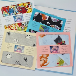 May include: Four handmade corner bookmarks featuring a cat theme. Each bookmark is made of fabric with a different cat print. The bookmarks have a small tag with the text "Just One More Chapter..." and "Slip onto page corner. Save your place."