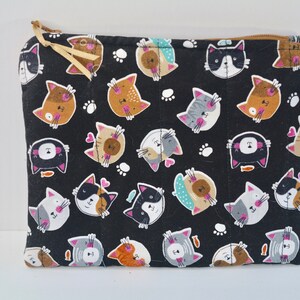 May include: Black zippered pouch with a repeating pattern of colourful cartoon cats on a black background. The cats have different facial expressions and are surrounded by white paw prints.