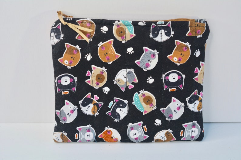 May include: Black zippered pouch with a repeating pattern of colourful cartoon cats on a black background. The cats have different facial expressions and are surrounded by white paw prints.