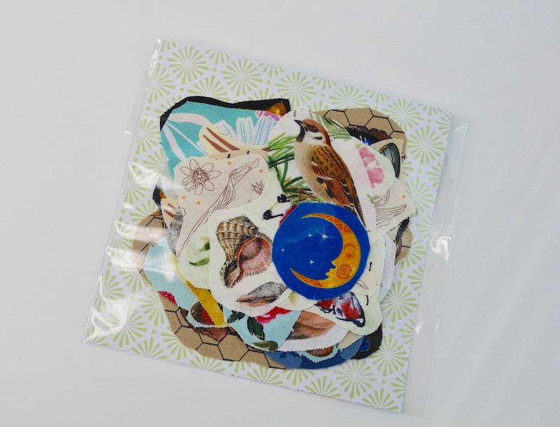 May include: A clear plastic bag containing a collection of fabric patches with nature-themed designs. The patches feature images of a bird, seashells, a crescent moon, and floral patterns. The background paper has a light green and white starburst pattern.