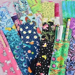 May include: A collection of colorful fabric pencil cases with different patterns, including floral, geometric, and abstract designs. Some cases have multiple pockets and are designed to hold pencils, pens, and other writing utensils.