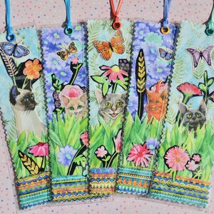 May include: Set of five decorative bookmarks featuring cat illustrations in a garden setting. Each bookmark has a unique cat breed, flowers, and butterflies. The bookmarks have a scalloped edge and colorful patterned trim with a ribbon for hanging.