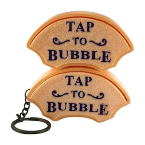 May include: Two fan-shaped, peach-colored keychains with the text "TAP TO BUBBLE" in navy blue. The keychains are connected by a small chain and a black keyring.