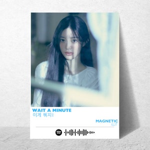May include: A blue and white poster with a woman's face in the background. The text on the poster reads "WAIT A MINUTE" in white letters and "이게 뭐지?" in black letters. Below the text is a Spotify logo and a barcode. The text "MAGNETIC" is in white letters and "ILLIT" is in black letters.
