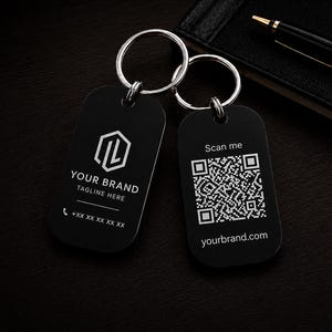May include: Two black rectangular keychains with rounded corners and silver metal rings. One keychain displays a white hexagonal logo, the text YOUR BRAND, TAGLINE HERE, and a phone icon with placeholders. The other features a QR code, Scan me, and yourbrand.com.