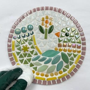 May include: A round mosaic art piece with a floral design. The mosaic is made of small, colorful tiles in shades of green, yellow, orange, and white. The piece is set on a white background.