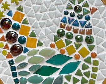 May include: A circular mosaic made of small glass and ceramic tiles in shades of green, yellow, orange, and brown. The tiles are arranged in a swirling pattern, creating a visually appealing design.