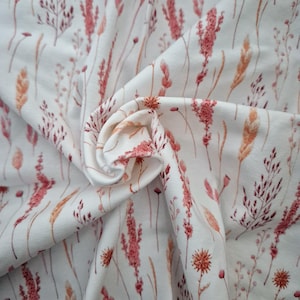 May include: White fabric with a repeating pattern of delicate, watercolour-style pink and orange wildflowers. The fabric is folded and draped, showing the pattern.