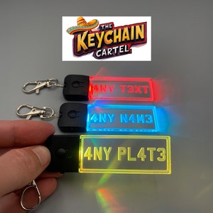 May include: Three LED keychain plates with different text. The top plate is red and says "ANY T3XT". The middle plate is blue and says "ANY N4M3". The bottom plate is yellow and says "ANY PL4T3".