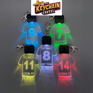 May include: Five LED light-up keychains shaped like football jerseys with different names and numbers. The keychains are green, blue, white, yellow, and red.