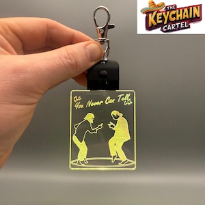 May include: A clear acrylic keychain with a light-up feature. The keychain features a silhouette of two people dancing with the text "You Never Can Tell" above them. The keychain is attached to a silver metal ring and a black plastic button.