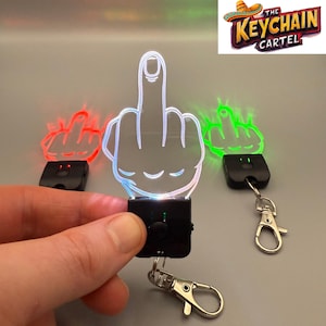 May include: A keychain with a light-up middle finger design. The keychain is black and has a silver metal ring. The middle finger is white and glows in the dark. The keychain is part of The Keychain Cartel.