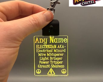 May include: A yellow LED keychain with the text "Any Name ELECTRICIAN AKA- Electrical Wizard Wire Whisperer Light Bringer Power Tripper Circuit Shaman" and a warning sign. The keychain has a silver metal ring and a black button.
