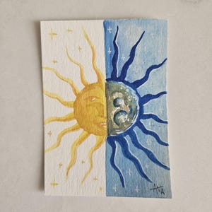 May include: Watercolor painting of the sun and moon, split vertically. The sun is yellow with a face, and the moon is blue with a face. Both sides have star accents. Signed "AVA" in the bottom right corner.