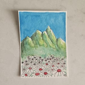 May include: Watercolor painting of a mountain range with a blue sky background. The mountains are green with black outlines. A field of white daisies with red centers is in the foreground. The painting is on a white paper.