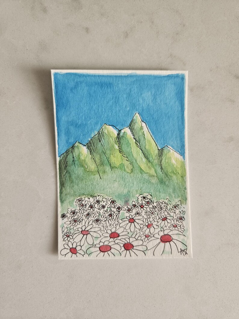 May include: Watercolor painting of a mountain range with a blue sky background. The mountains are green with black outlines. A field of white daisies with red centers is in the foreground. The painting is on a white paper.