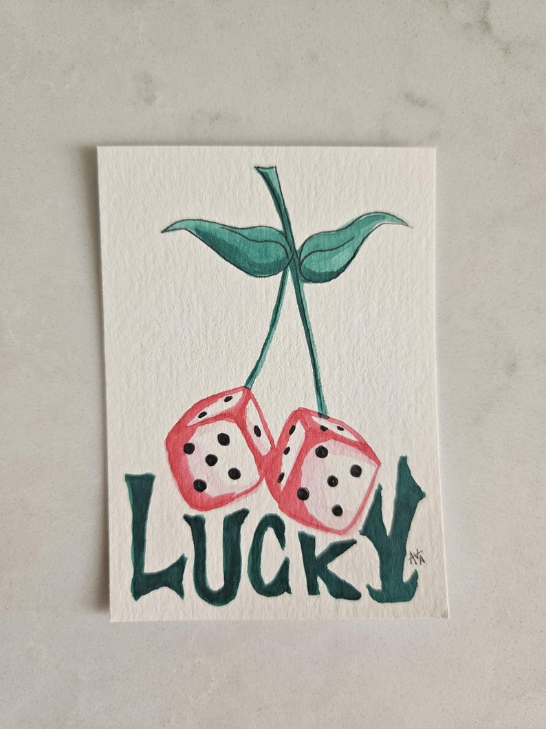May include: Watercolor painting of two red dice with black dots, resembling cherries, connected by a green stem and leaves. The word "LUCKY" is written in green below the dice, creating a playful and whimsical design.