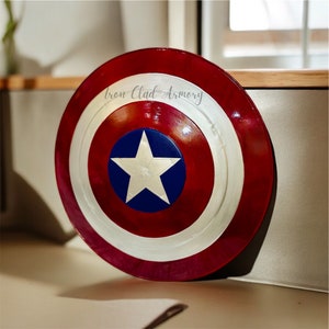 Pu&ograve; includere: Uno scudo di Capitan America rosso, bianco e blu con una stella bianca su sfondo blu. Lo scudo ha la scritta "Iron Clad Armory".