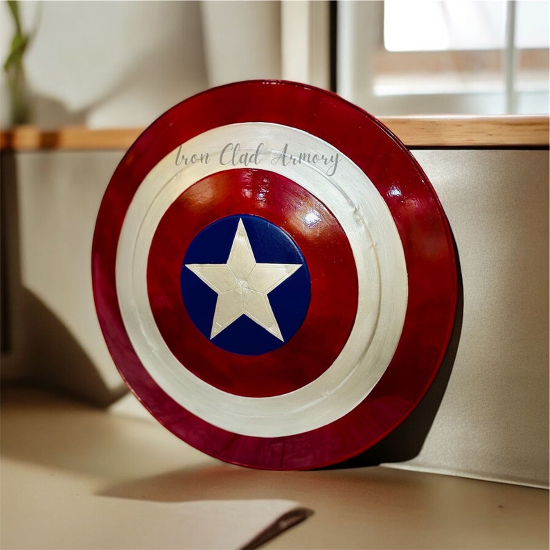 Pu&ograve; includere: Uno scudo di Capitan America rosso, bianco e blu con una stella bianca su sfondo blu. Lo scudo ha la scritta "Iron Clad Armory".
