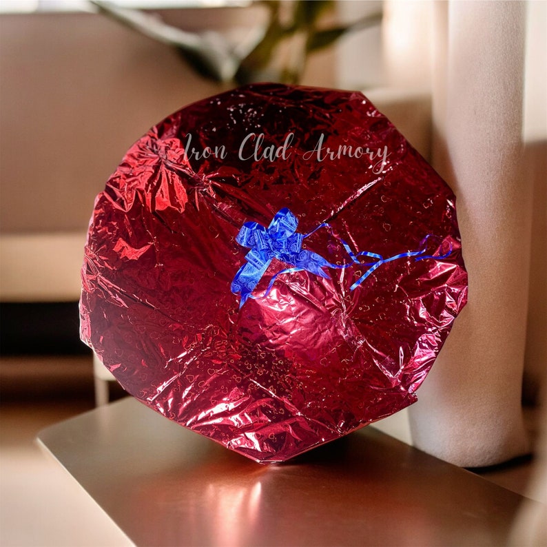 Pu&ograve; includere: Una barretta di cioccolato avvolta in carta stagnola rossa con un nastro blu e la scritta "Iron Clad Armory" stampata sul davanti.