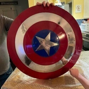 May include: A red, white, and blue Captain America shield with a silver star in the center. The shield is made of metal and has a shiny finish.