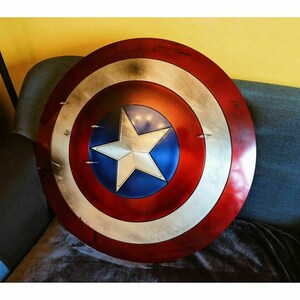 May include: A red, white, and blue Captain America shield with a five-pointed star in the center. The shield has a distressed, weathered look.