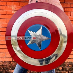 May include: A red, white, and blue Captain America shield with a silver star in the center. The shield is held by a person wearing blue jeans.