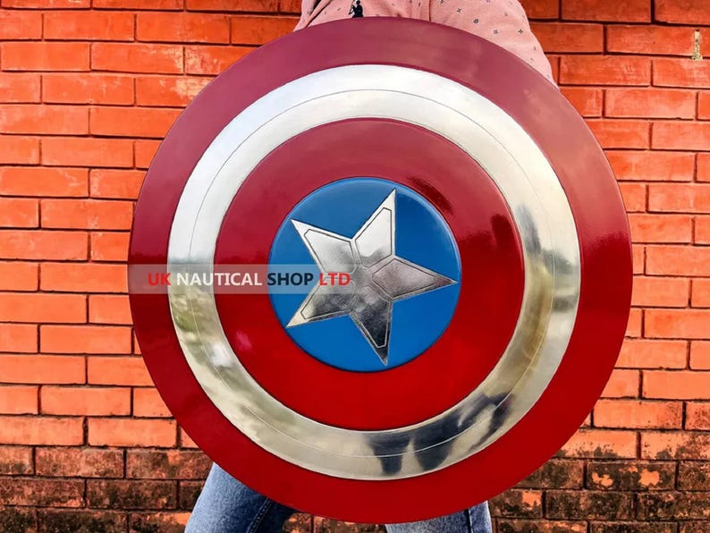 May include: A red, white, and blue Captain America shield with a silver star in the center. The shield is held by a person wearing blue jeans.