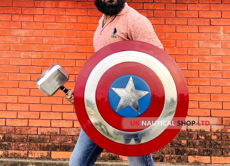 May include: A person holding a silver and black Thor's hammer and a red, white, and blue Captain America shield. The shield has a large silver star in the center. The text "UK NAUTICAL SHOP LTD" is visible on the shield.