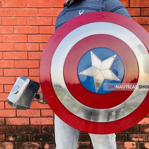 May include: A person holding a red, white, and blue Captain America shield with a silver star in the center. The shield is about 2 feet in diameter. The person is also holding a silver hammer.