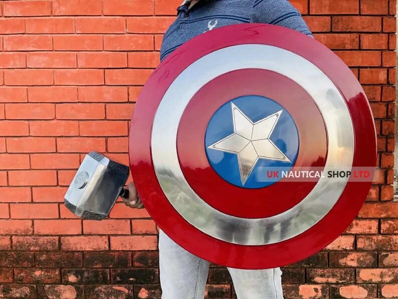 May include: A person holding a red, white, and blue Captain America shield with a silver star in the center. The shield is about 2 feet in diameter. The person is also holding a silver hammer.